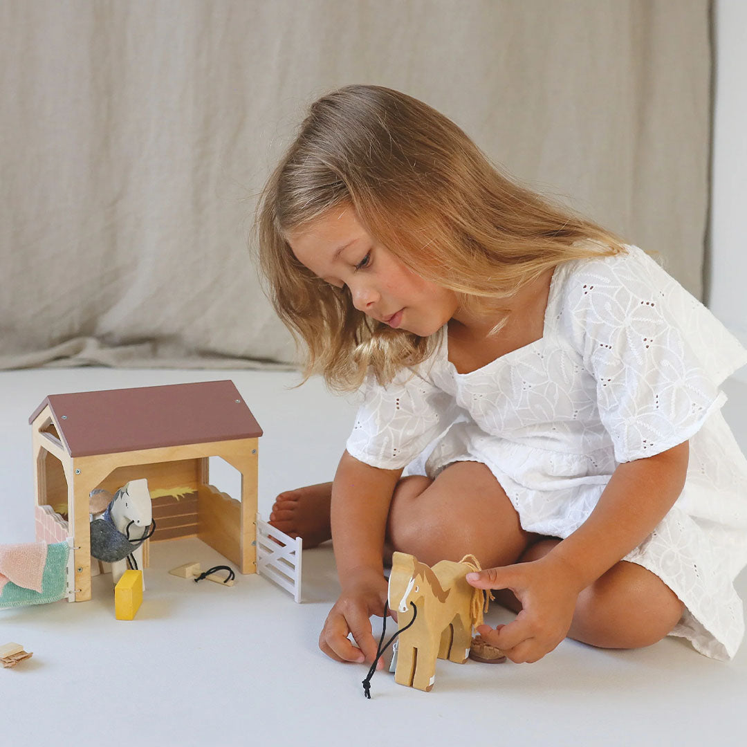 Meisje speelt op de grond met de Tender Leaf Toys houten paardenstal speelset.