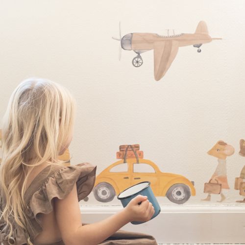 Een kind kijkt naar een muur met een That's Mine retro vliegtuig muursticker en andere reisstickers.