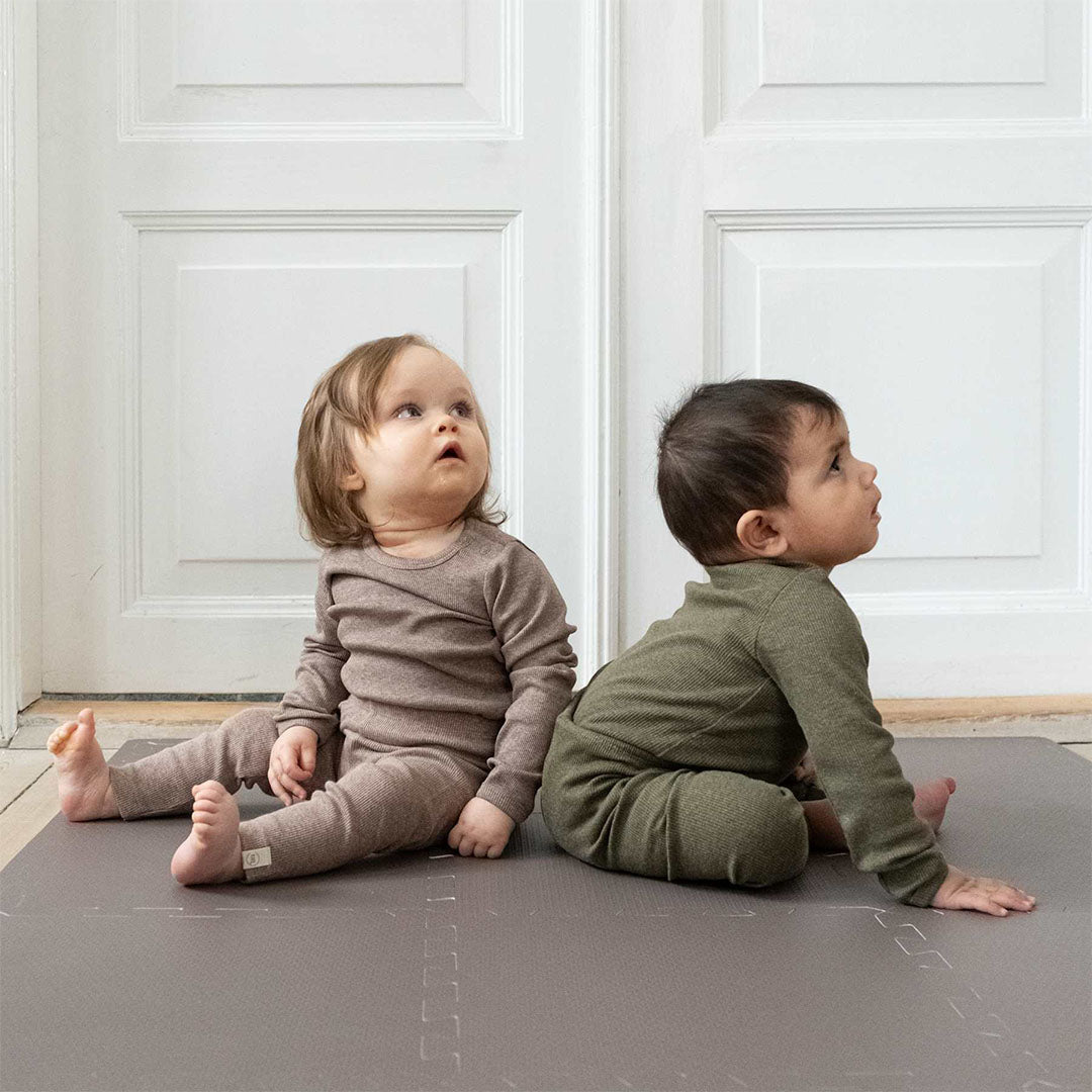 Twee baby's zitten op een bruine that's mine schuim speelmat voor baby's.