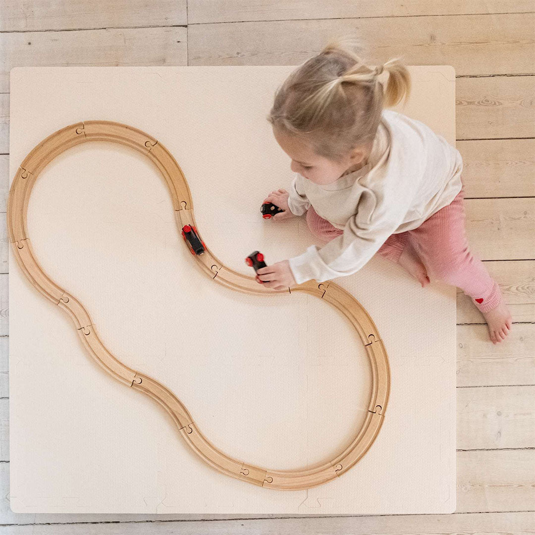 Een peuter speelt met een houten treinbaan op de that's mine beige foam speelmat, van bovenaf gezien.