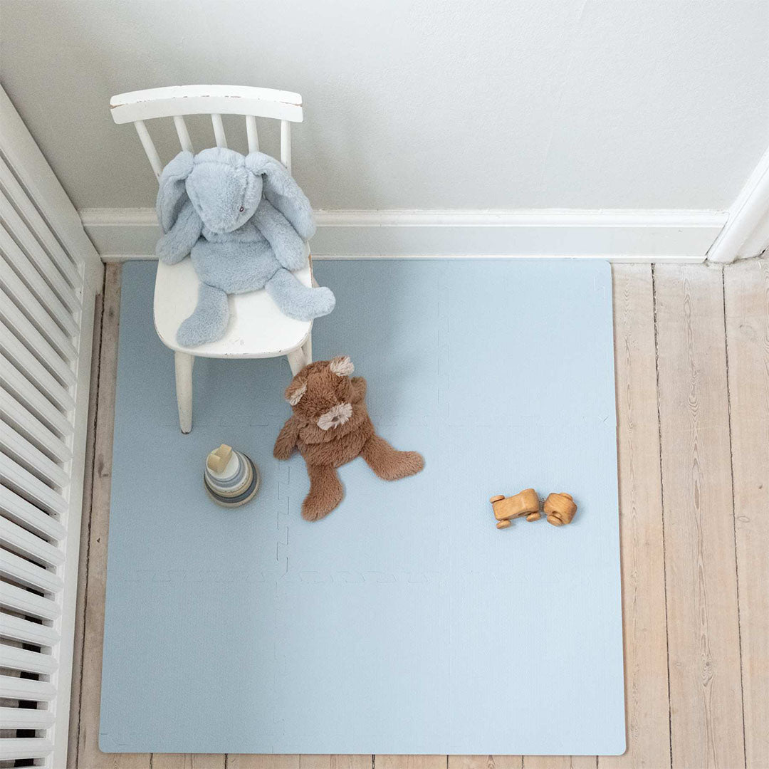 that's mine lichtblauwe foam speelmat voor baby's op een houten vloer, met een knuffelkonijn en ander speelgoed erop.