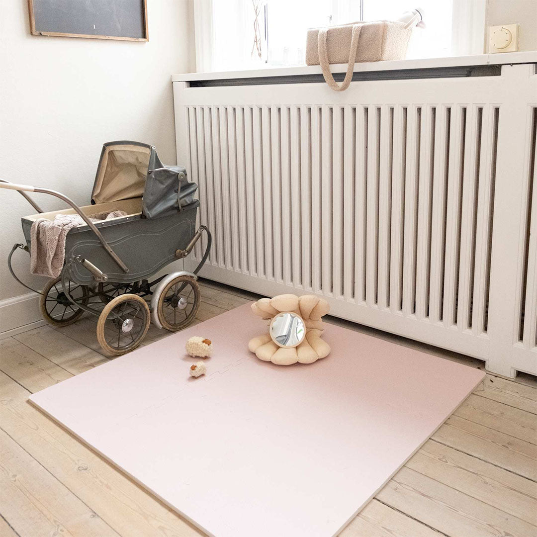 Een roze foam speelmat ligt op een houten vloer met een kinderwagen ernaast.