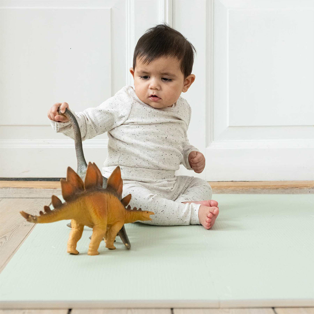 Een baby zit op de that's mine sage green foam speelmat en speelt met twee dinosaurus speelgoedfiguren.