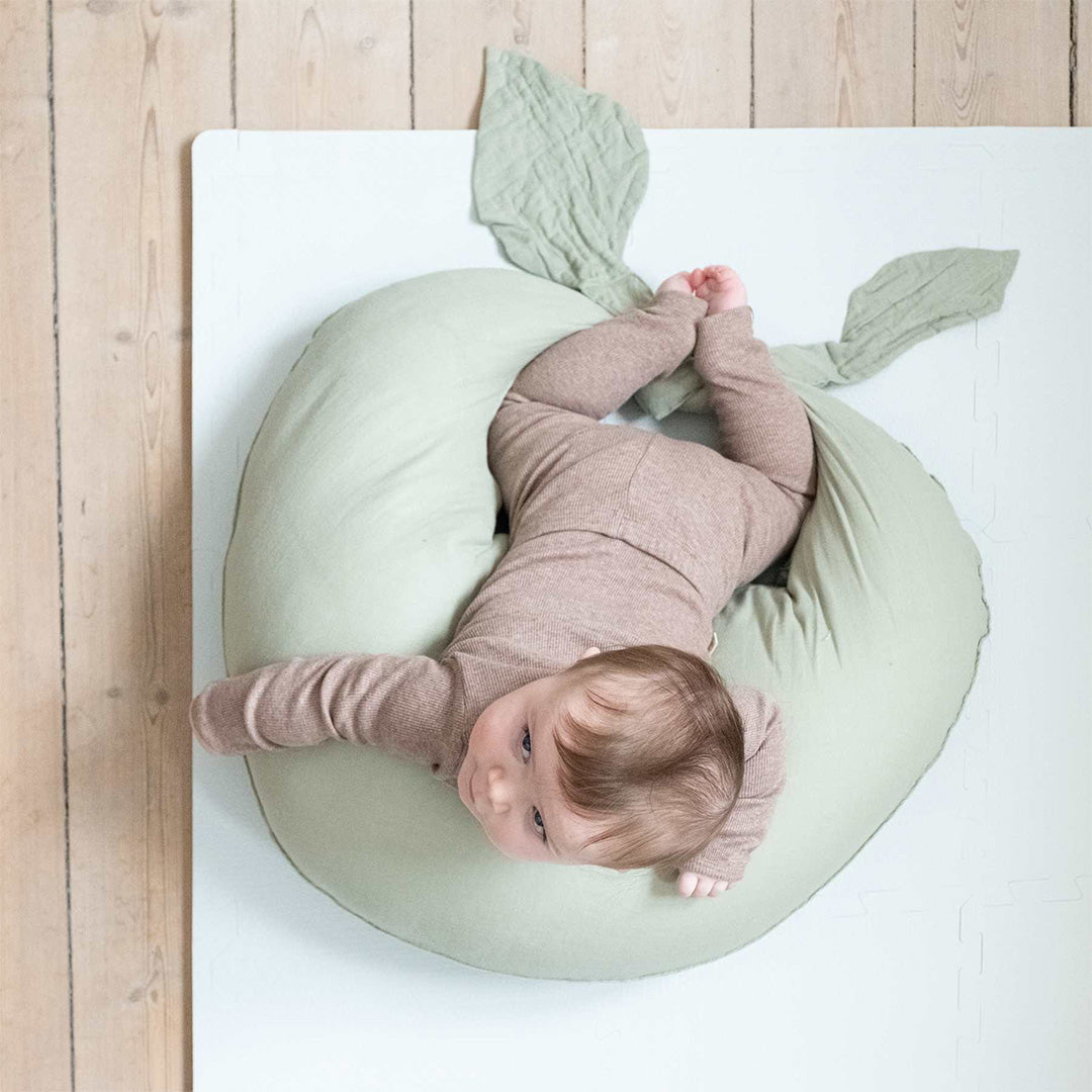 Een baby ligt op een lichtgroen kussen op een that's mine sky blue foam speelmat op een houten vloer.