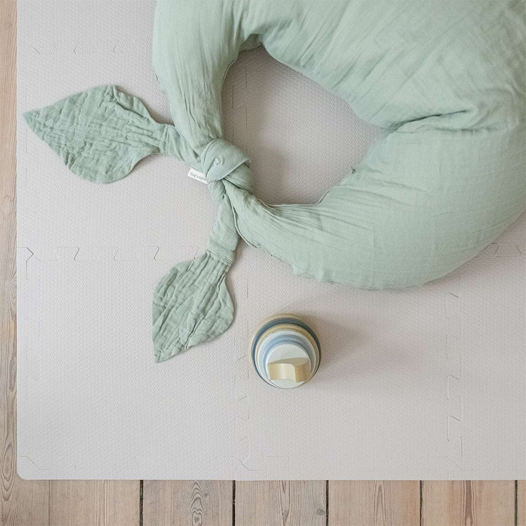 Een deel van de zachtbruine That's Mine schuim speelmat met een groen babykussen en een houten stapeltoren.