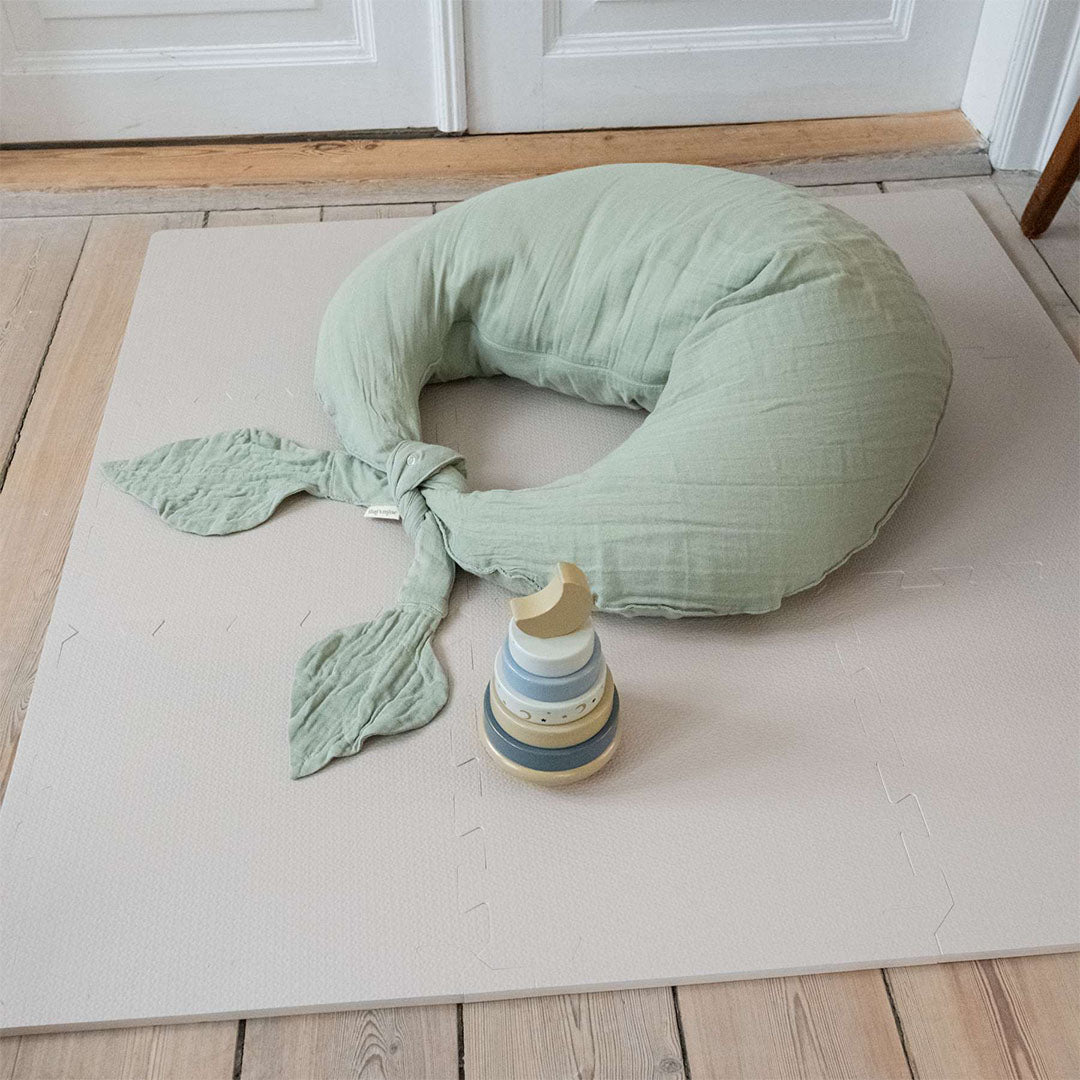 De zachtbruine That's Mine schuim speelmat op een houten vloer met een groen babykussen en een houten stapeltoren.
