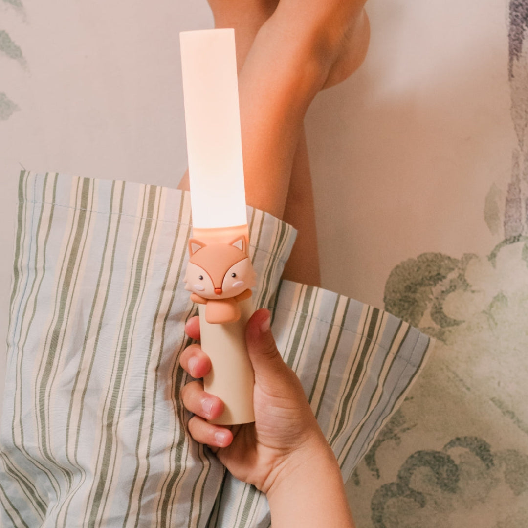 Een kinderhand houdt de oplichtende kinderlamp met vosje vast in bed.