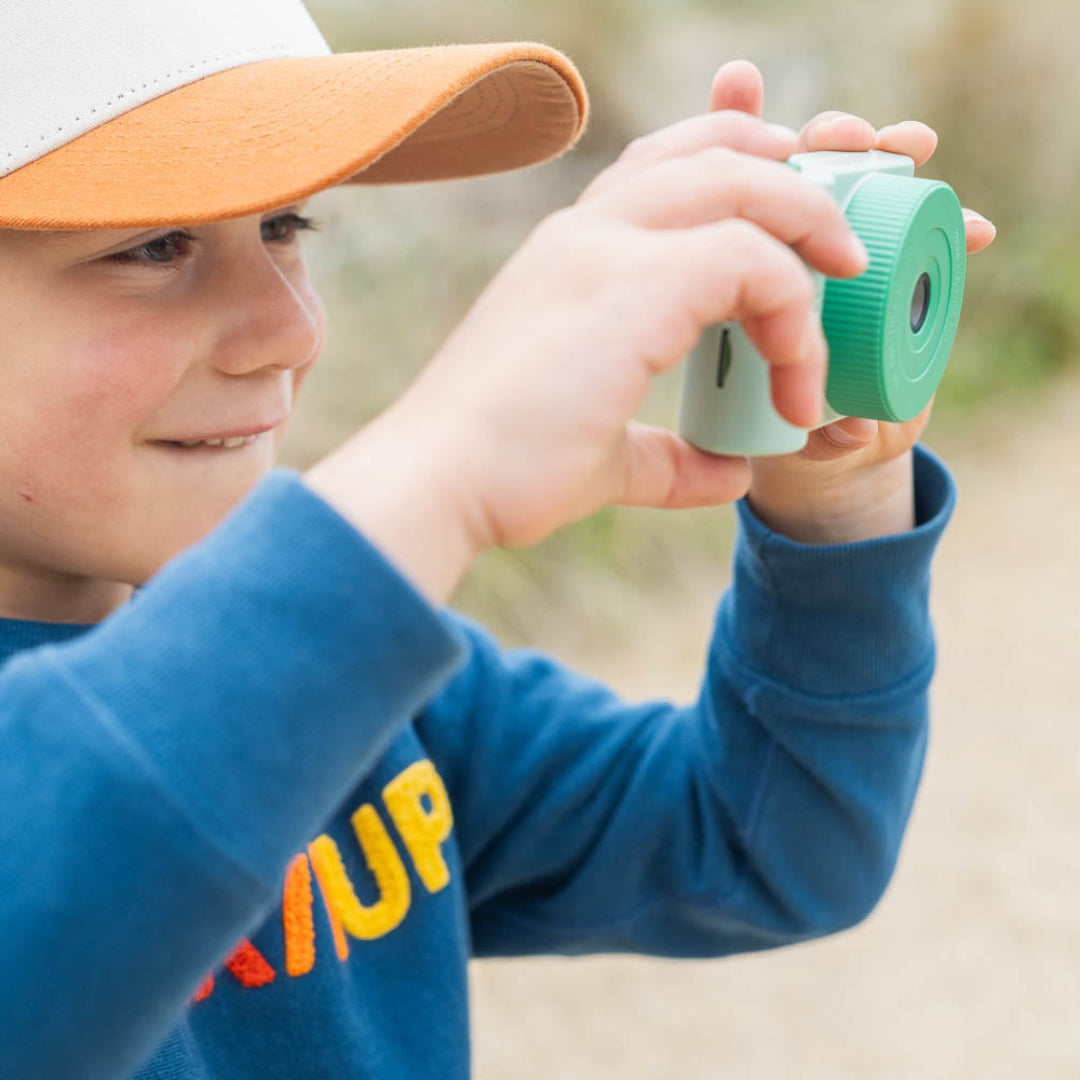 Een kind houdt de groene the zoofamily kindercamera vast en kijkt opzij, klaar om een foto te maken.