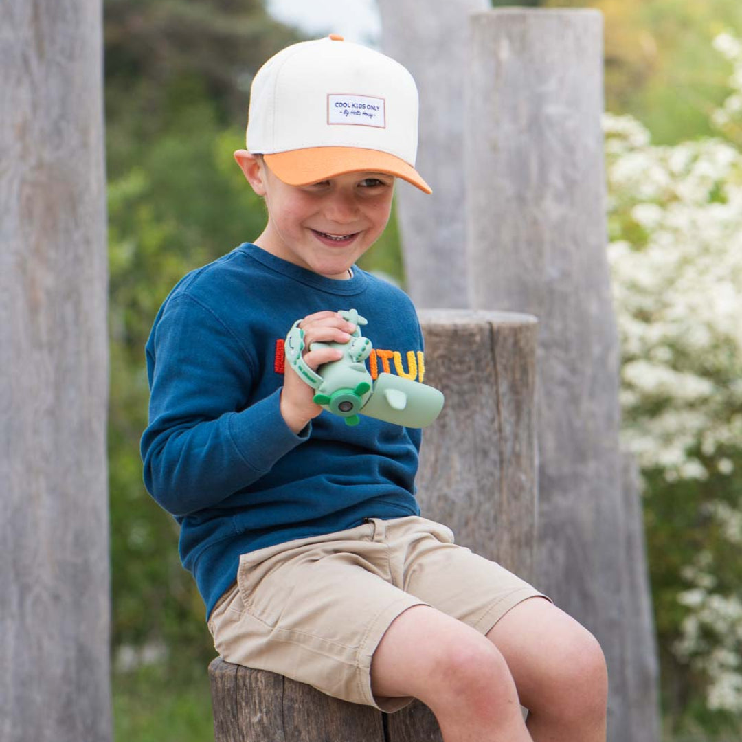 Een jongen zit op een boomstronk en houdt de groene the zoofamily kindervideocamera vast.