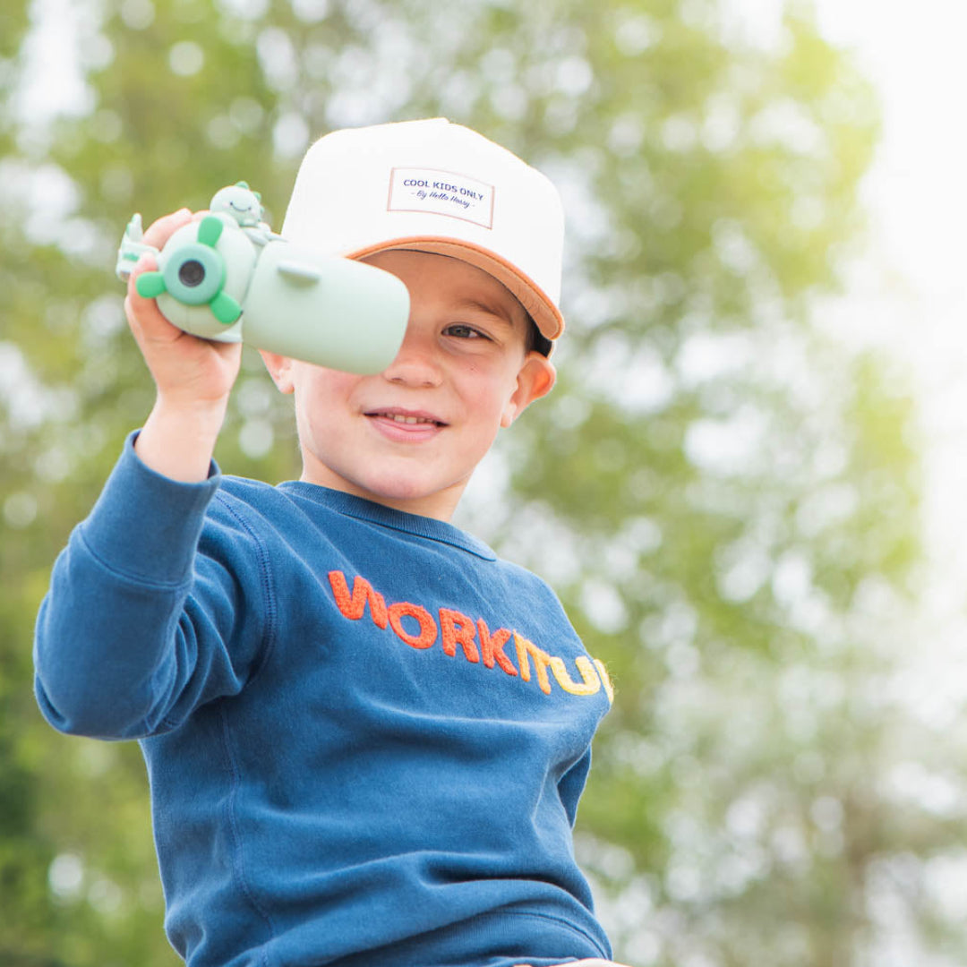 Een lachende jongen kijkt door de groene the zoofamily kindervideocamera in de buitenlucht.