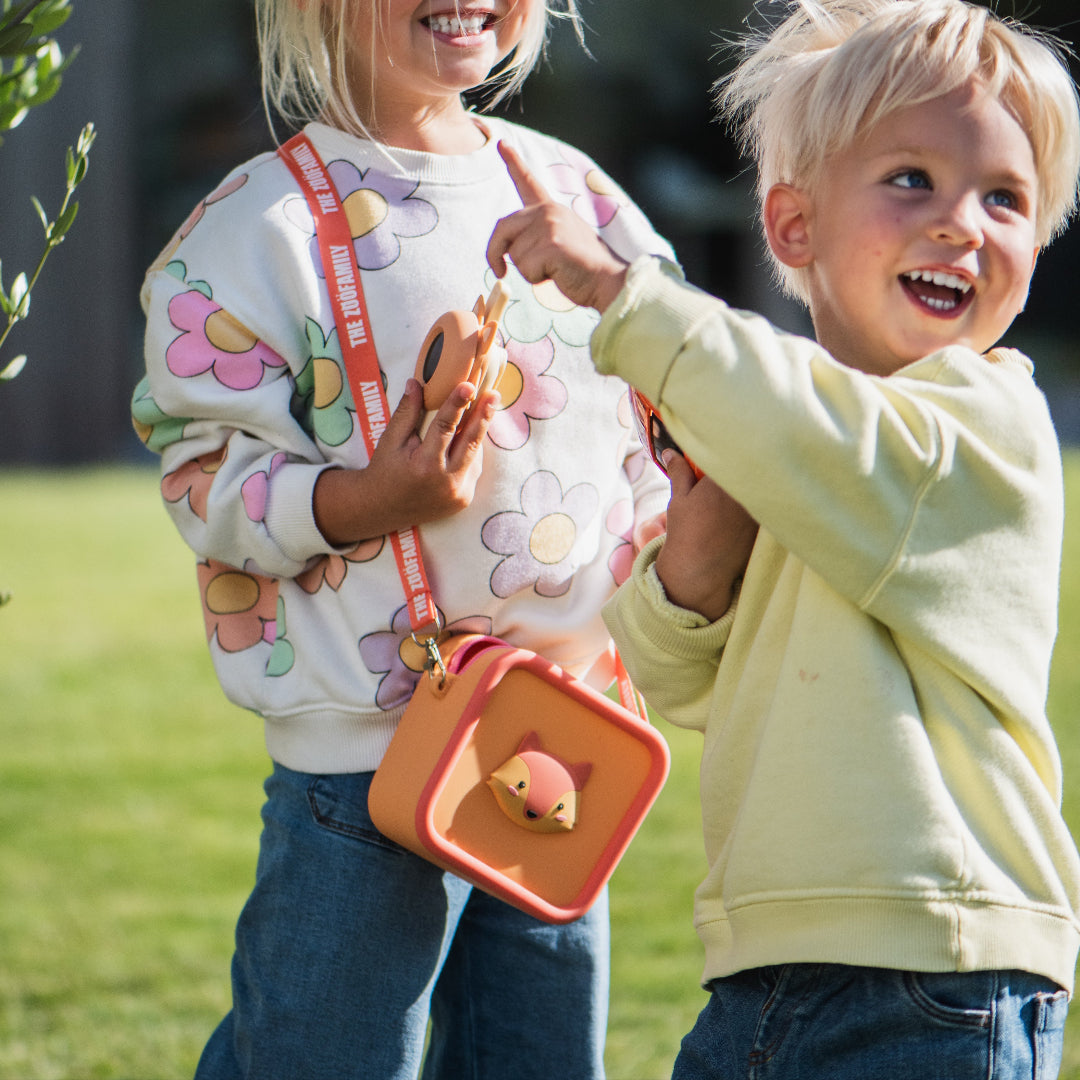 Twee lachende kinderen buiten, waarvan één de the zoofamily kinderschoudertas met vosgezicht draagt.