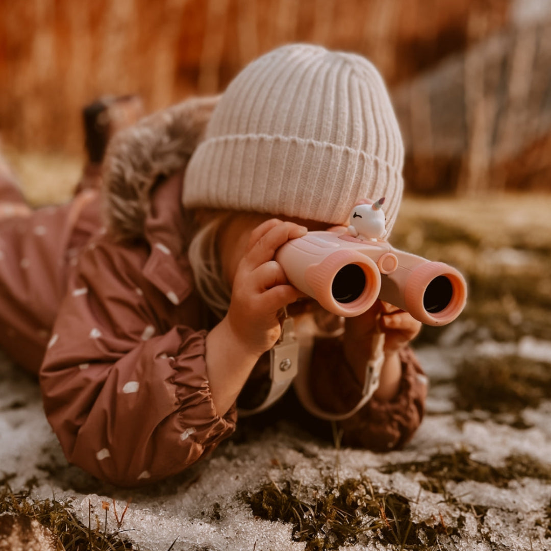 Een kind ligt op de grond en kijkt door de roze eenhoorn kinderverrekijker.