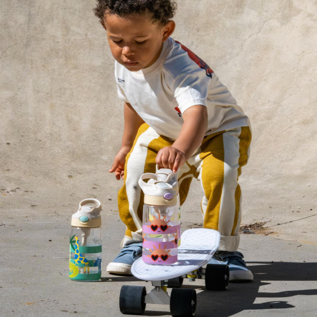 Een kind op een skateboard houdt de The Cotton Cloud kinder waterfles met zonnetjes vast, met een andere fles ernaast.