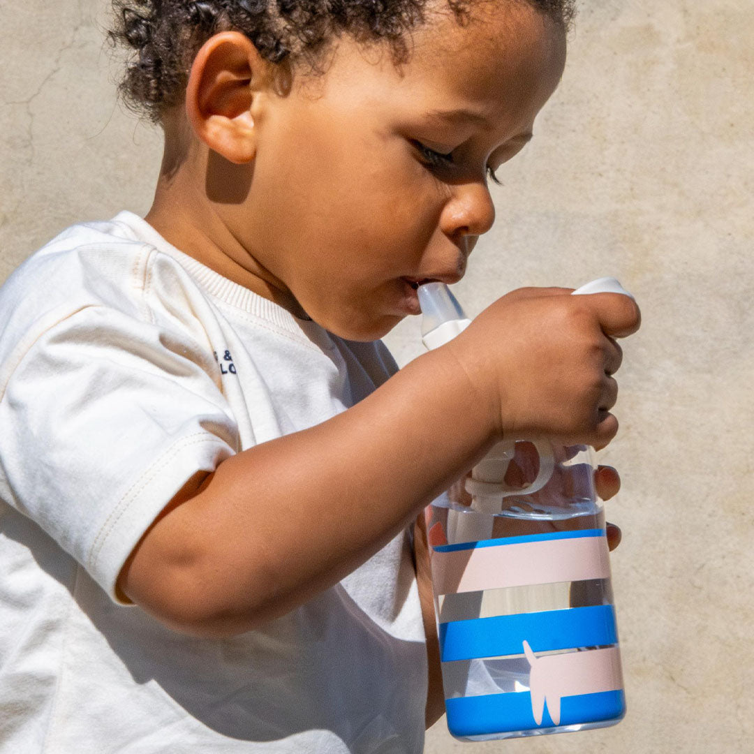 Een kind drinkt uit de the cotton cloud drinkfles met gestreepte print en cartoonhonden.