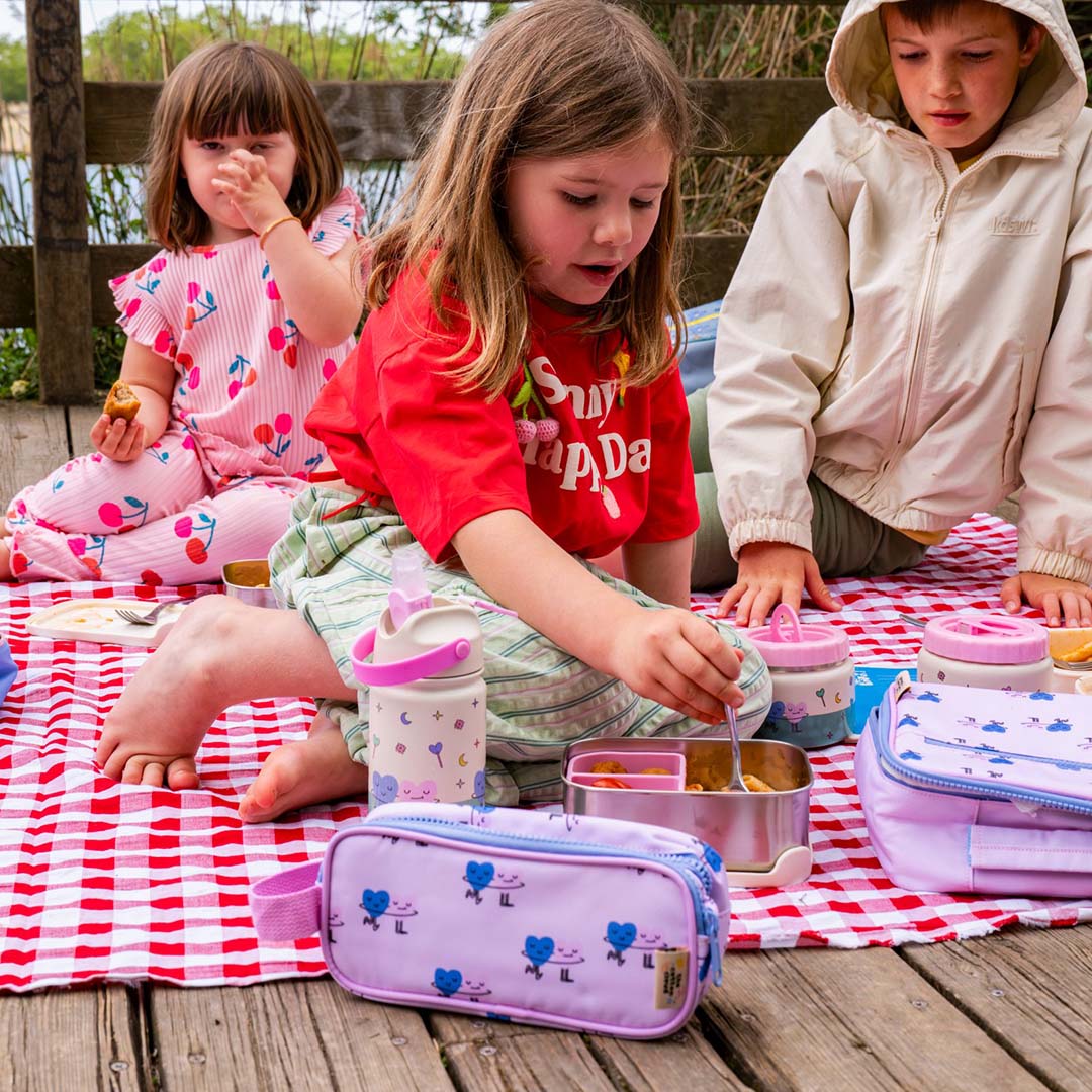 Drie kinderen picknicken met een paarse etui met dansende harten en bijpassende lunchspullen.