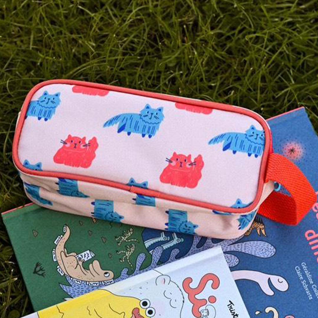 The Cotton Cloud roze etui met kattenpatroon liggend op gras tussen kinderboeken.