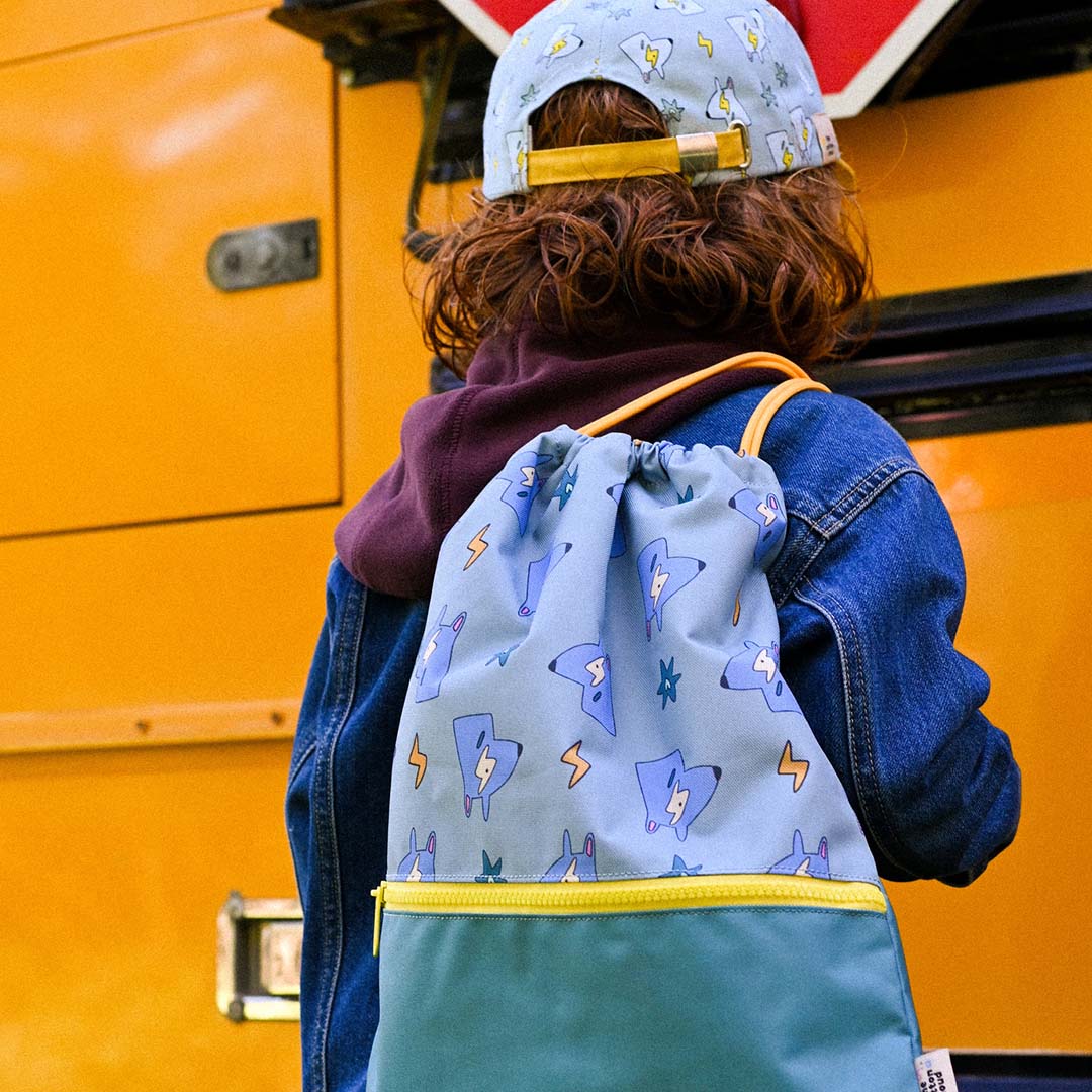 Een kind draagt de the cotton cloud gym- en zwemtas met funky dogs op de rug, staand bij een gele schoolbus.