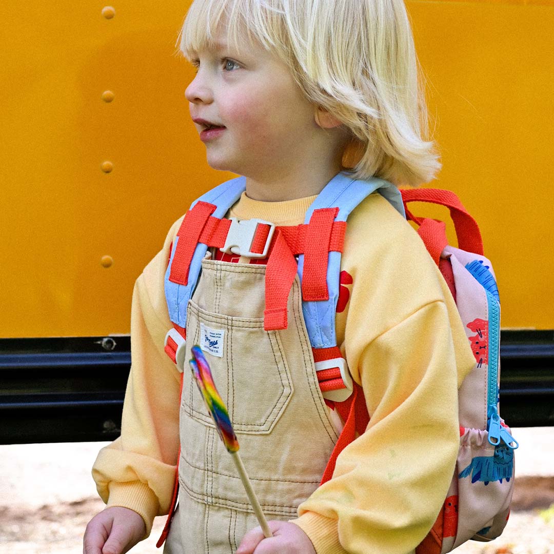 Een kind met de the cotton cloud kleuterrugzak met kattenprint op de rug, staand voor een gele schoolbus.