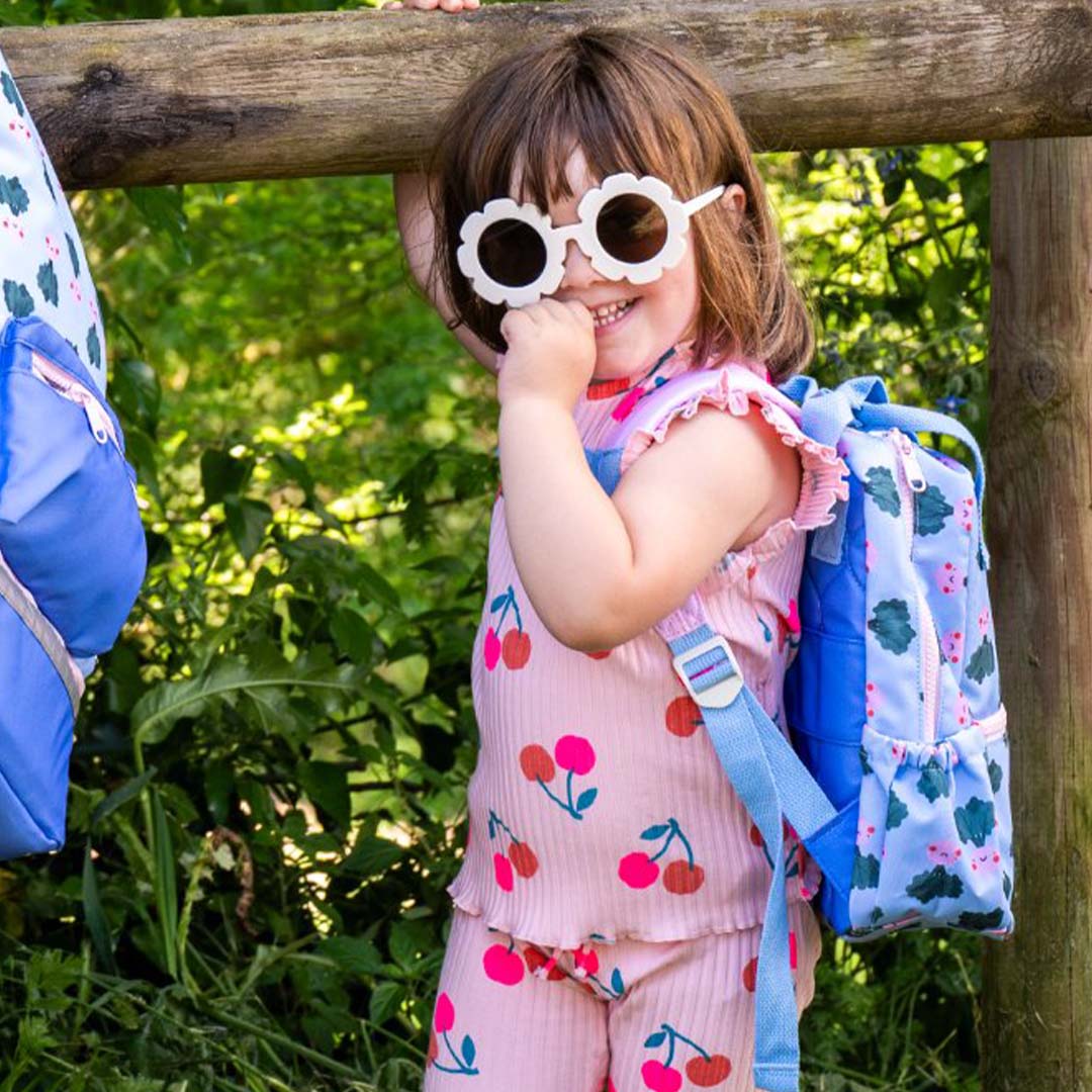 Een lachend kind draagt de the cotton cloud kleuterrugzak met 'veggie pals' patroon buiten.