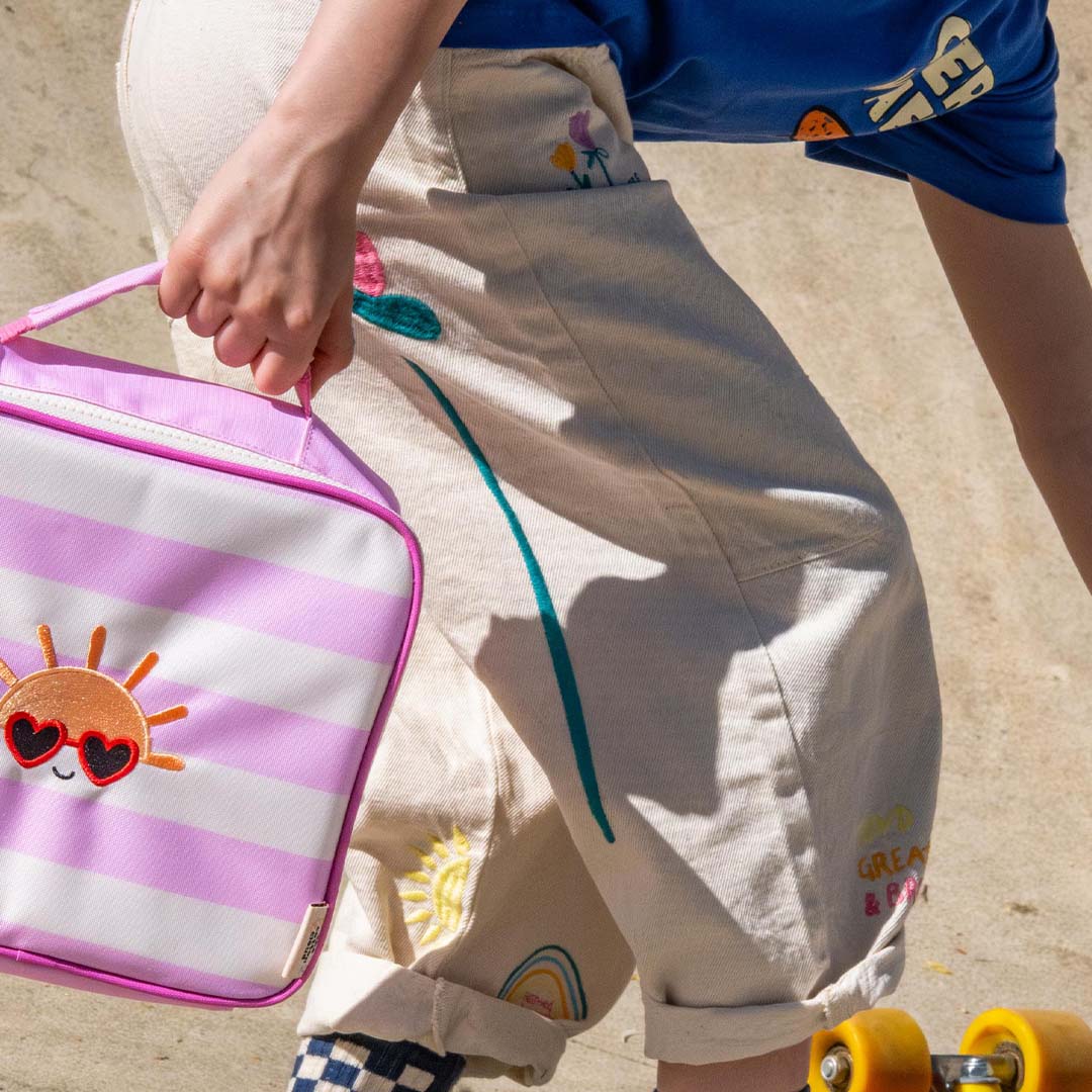 The Cotton Cloud roze gestreepte koeltas met zonnetje, vastgehouden door een persoon op een skateboard.