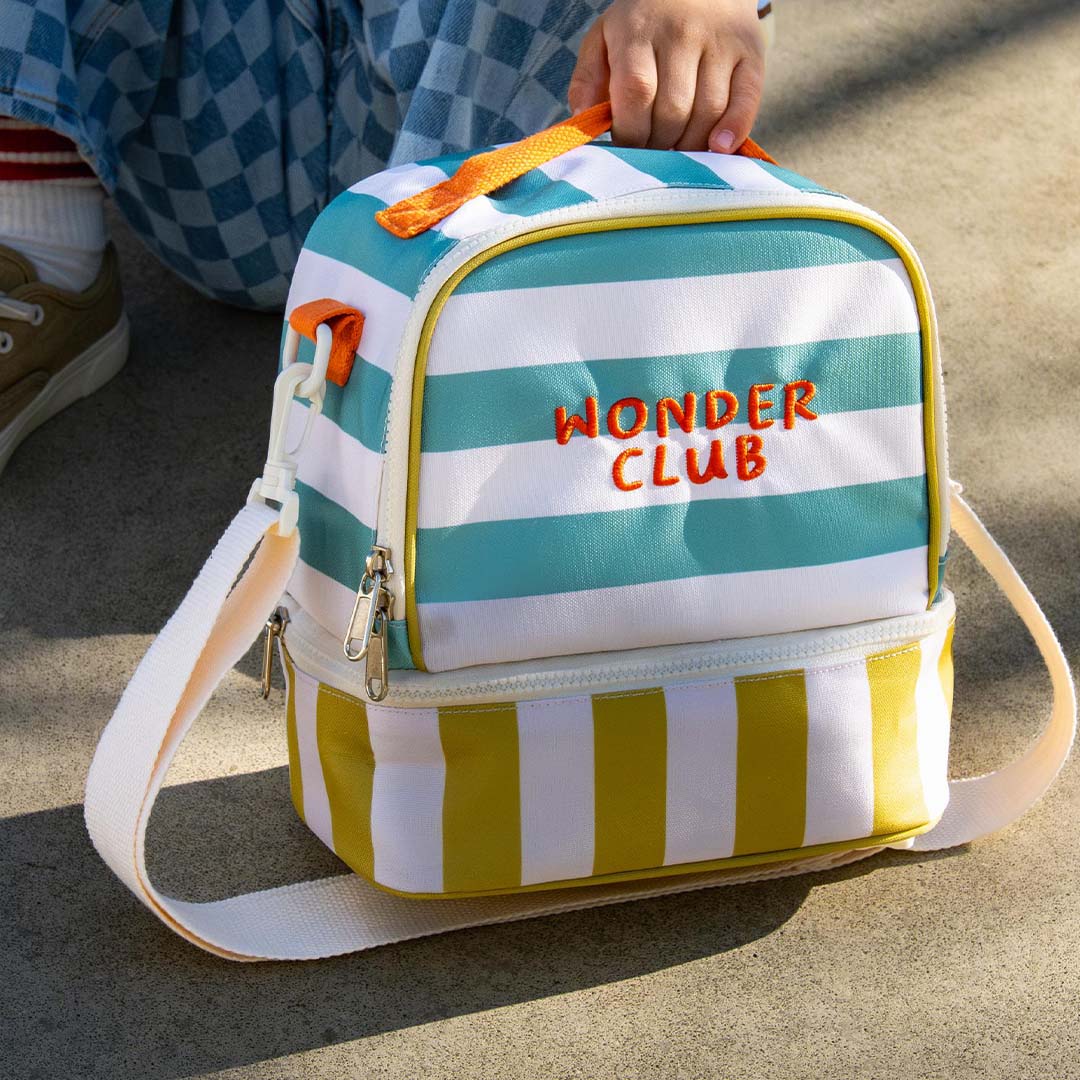 Detail van de the cotton cloud gestreepte koeltas met 'Wonder Club' tekst en een kinderhand die het oranje handvat vasthoudt.