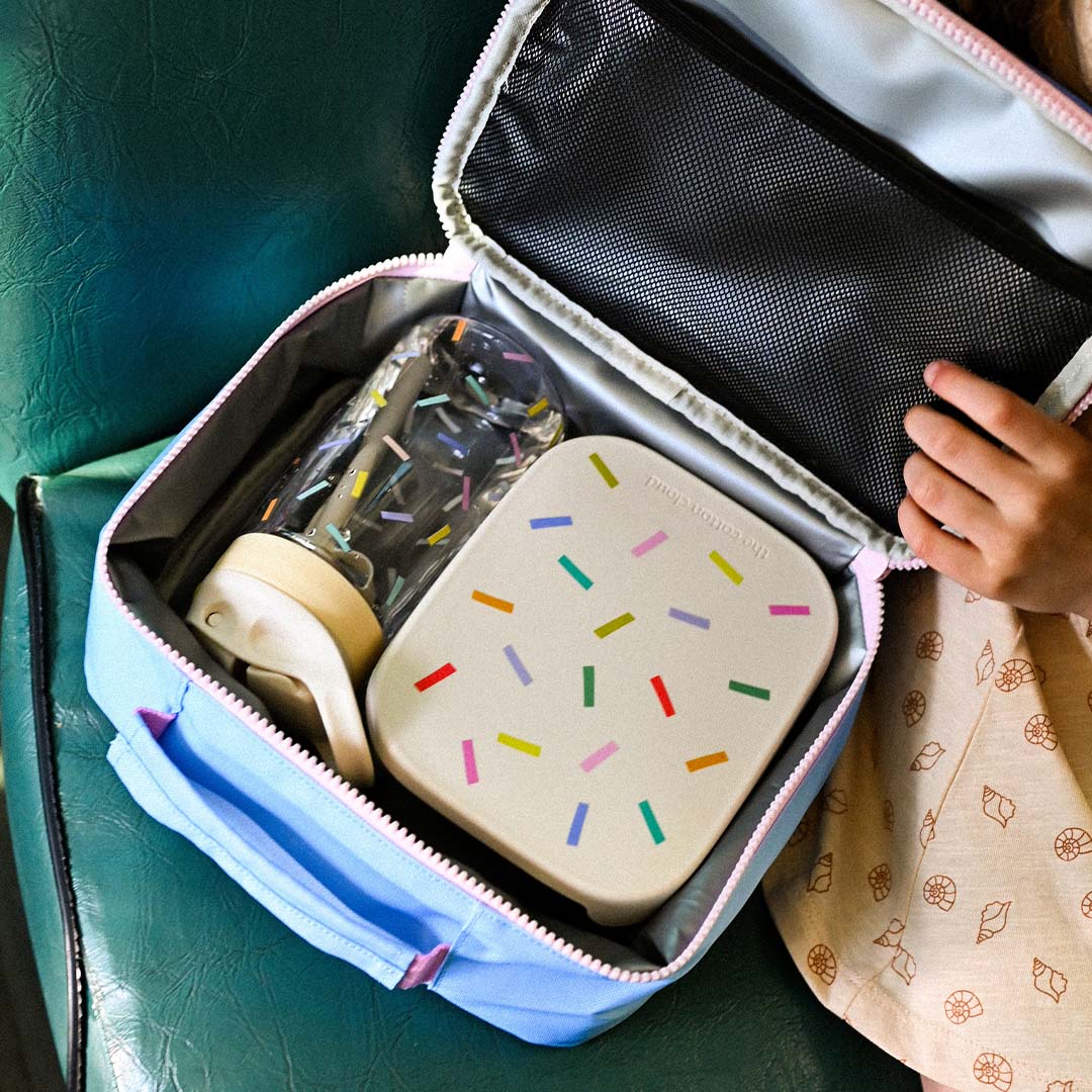 Een open lichtblauwe koeltas met daarin een drinkfles en een lunchbox met gekleurde spikkels.