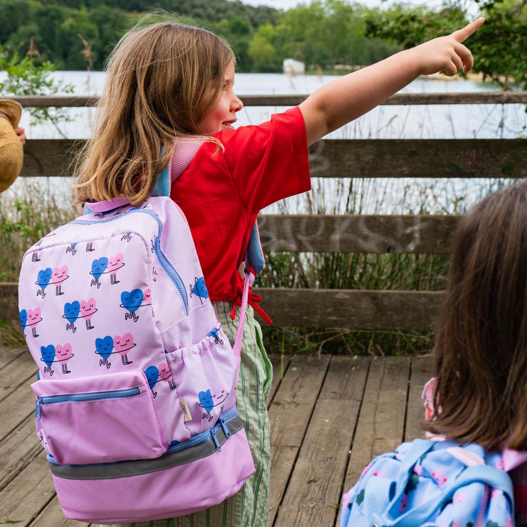 Een kind met de roze schoolrugzak met hartenpatroon wijst naar een meer.
