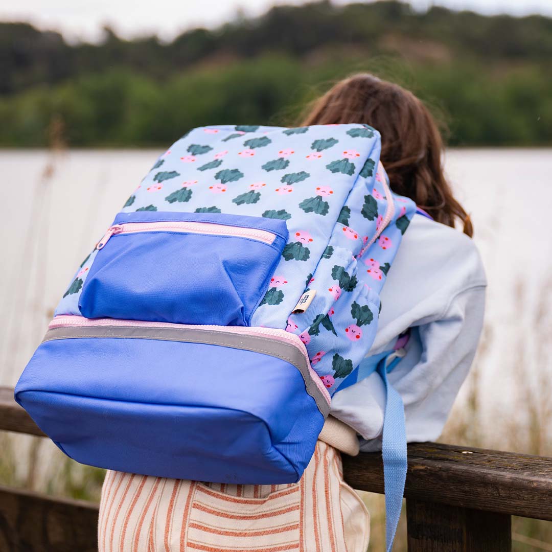 Een kind draagt de The Cotton Cloud schoolrugzak met 'veggie pals' patroon, gezien van achteren bij een meer.