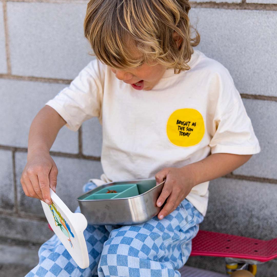 Een kind op een skateboard opent de the cotton cloud kinderbroodtrommel met safari dierenpatroon.