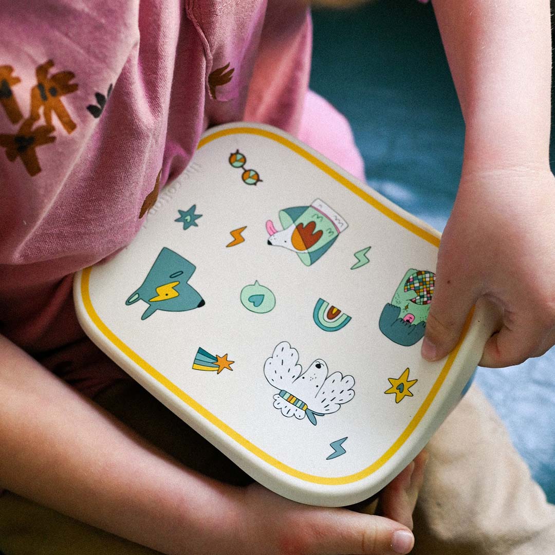 Een kind houdt de gesloten The Cotton Cloud kinder broodtrommel met funky hondenpatroon vast.