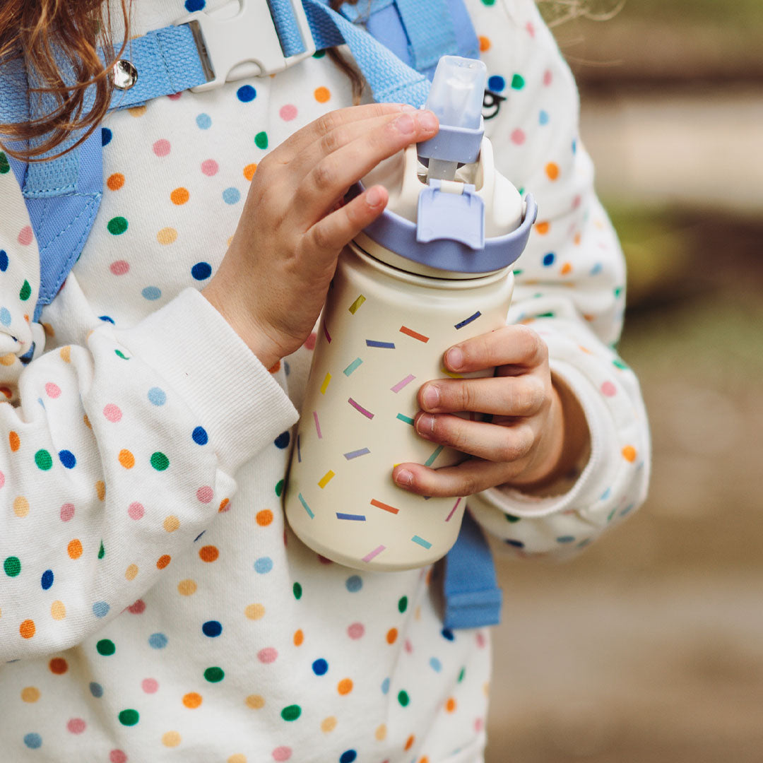 Kinderhanden openen de The Cotton Cloud drinkfles met confetti patroon.