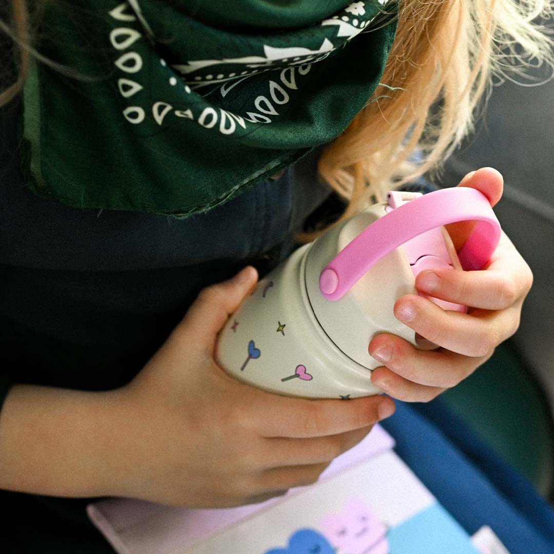 Een kind houdt de The Cotton Cloud kinder drinkfles met harten en sterren vast.