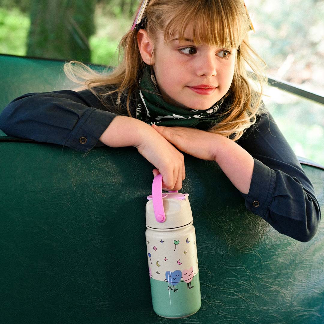 Een meisje zit in een voertuig en houdt de The Cotton Cloud kinder drinkfles met harten en sterren vast.