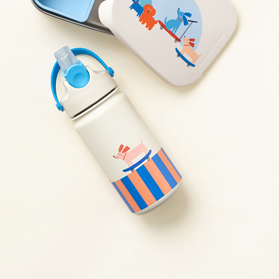 De the cotton cloud rvs drinkfles met een hond op skateboard en gestreepte print, naast een lunchbox.