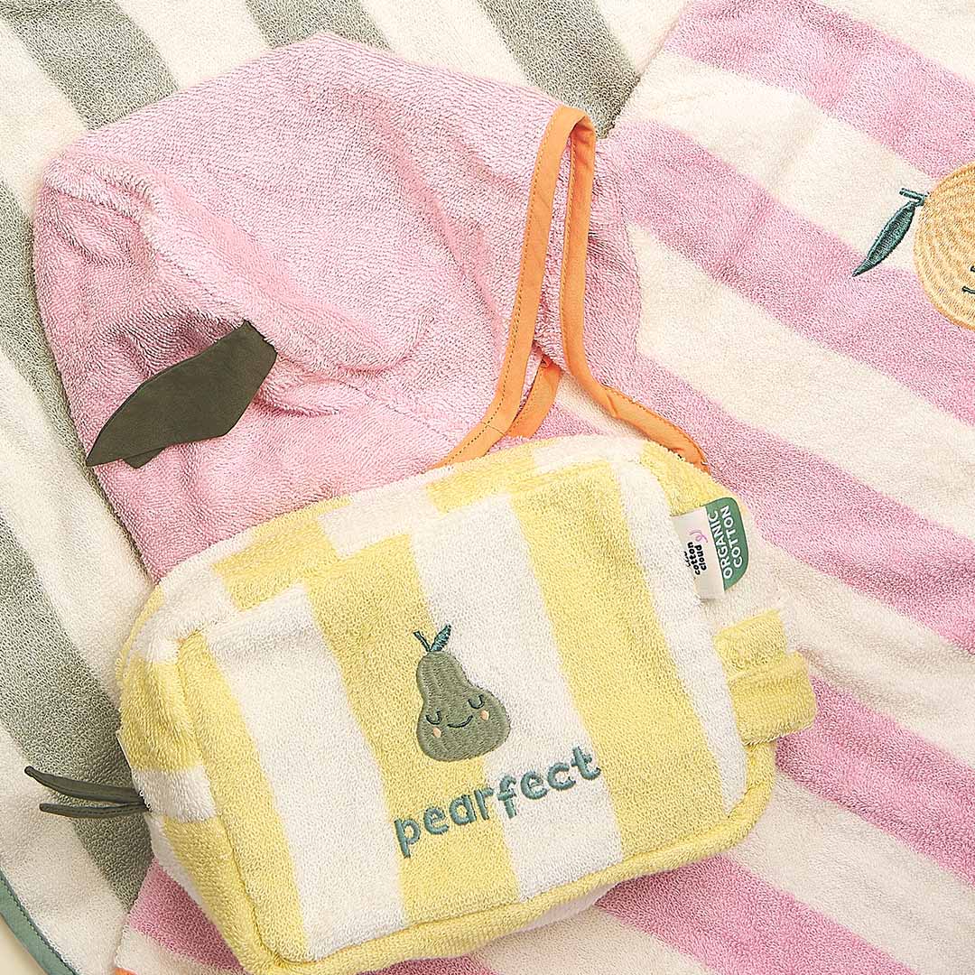 the cotton cloud toilettas met gele en witte strepen en een peer, liggend tussen een roze gestreepte handdoek en een roze badcape.