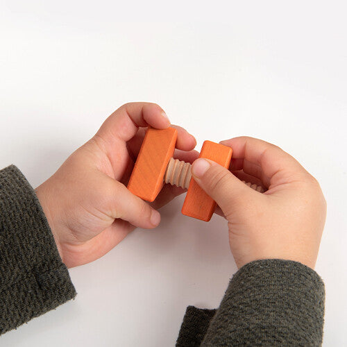 Kinderhanden schroeven een oranje houten bout en moer van het tickit speelgoed in elkaar.