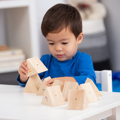 Een kind speelt met Tickit houten geluiden memorie prismablokken op een witte tafel.