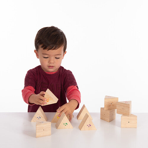 Een kind speelt met Tickit houten geluiden memorie prismablokken op een witte ondergrond.