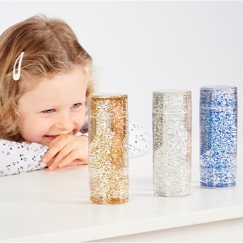 Een meisje kijkt aandachtig naar drie glittercilinders op een witte tafel.