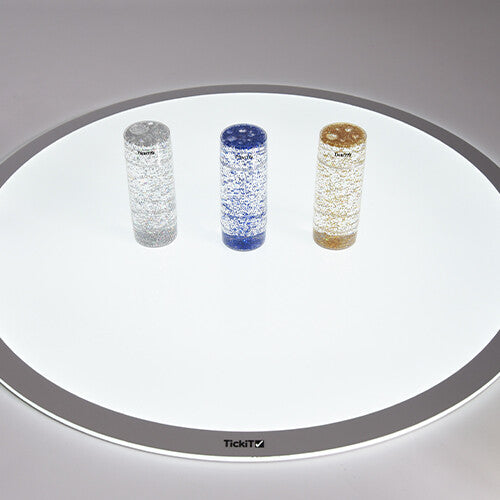 Drie Tickit glittercilinders staan op een grote ronde witte lichttafel.