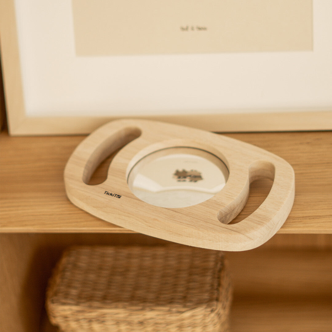 De Tickit houten lachspiegel met handgrepen ligt op een houten plank.
