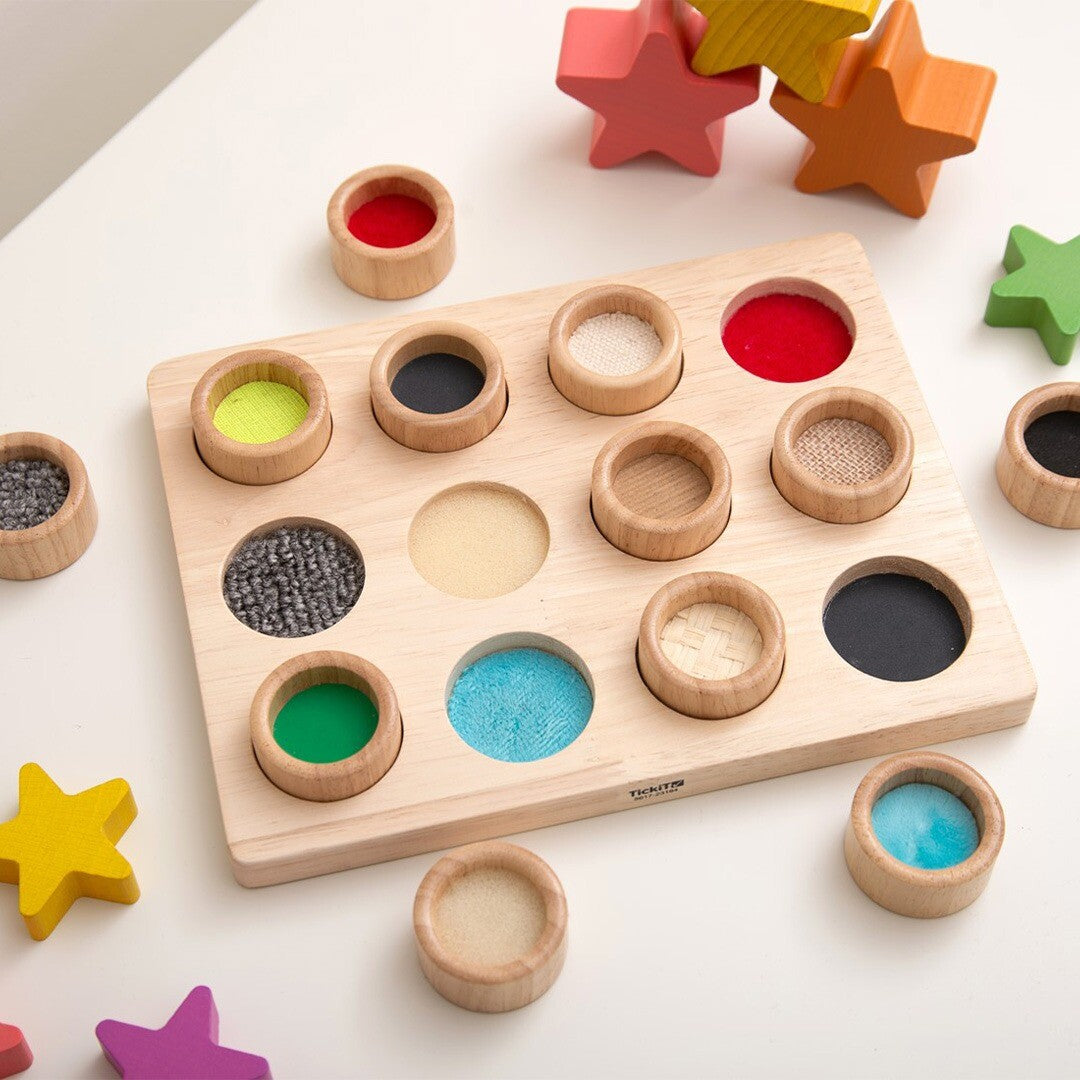Tickit sensorisch sorteerspel met houten bord en cups met diverse texturen en kleuren, omringd door kleurrijke houten sterren.