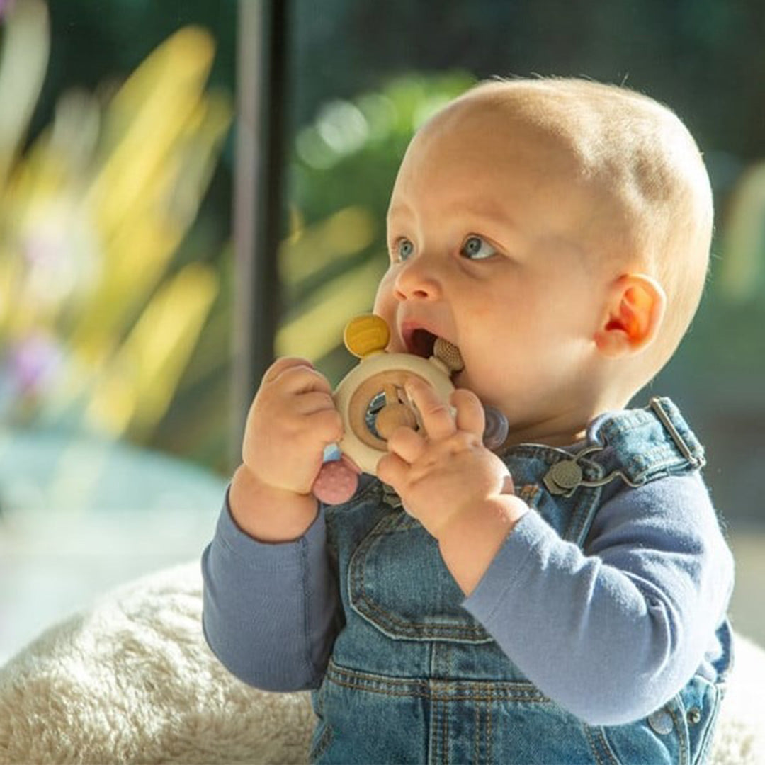 Een baby in een spijkerbroekje kauwt op de tickit silisoft bijtring en rammelaar.