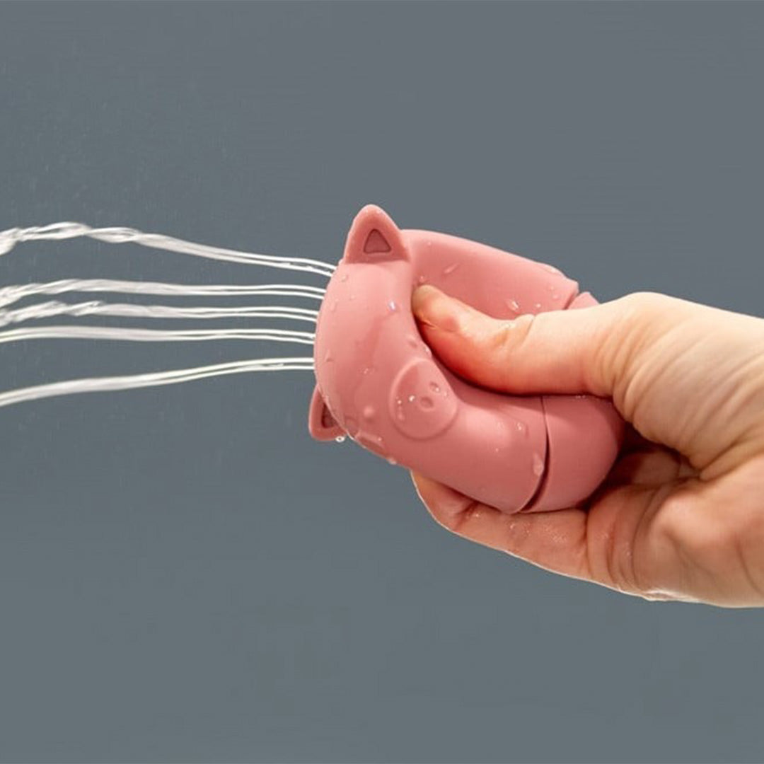 Een hand knijpt in een roze varken-vormige waterspuiter, waar water uit spuit.