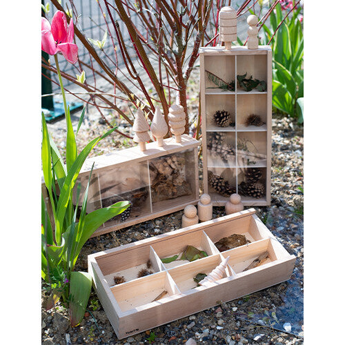 Drie houten Tickit sorteerbakken in een tuin, gevuld met natuurlijke materialen zoals dennenappels en bladeren.