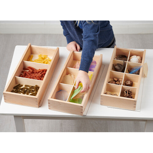 Drie houten Tickit sorteerbakken op een tafel, gevuld met pasta, bladeren en natuurlijke materialen.