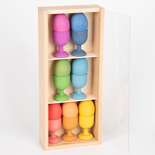 Een verticale houten Tickit sorteerbak met drie planken, gevuld met gekleurde houten eierdopjes en eieren.