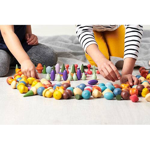 Twee kinderen spelen met de Tickit houten speelfiguren in diverse vormen en kleuren op een houten vloer.