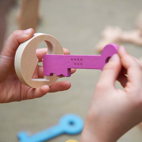 Twee handen houden een houten ring en een paarse houten sleutel met stippen vast.