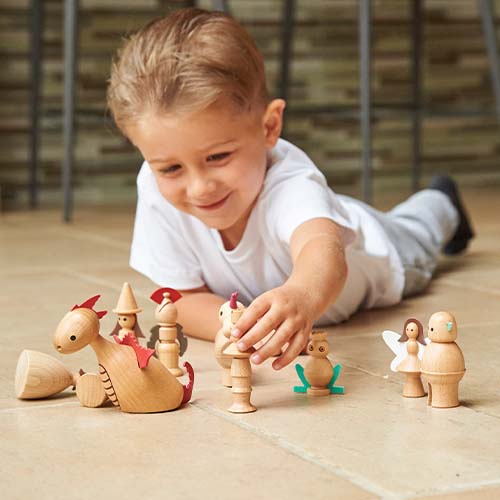 Een jongen ligt op de vloer en speelt met de tickit houten sprookjesfiguren.